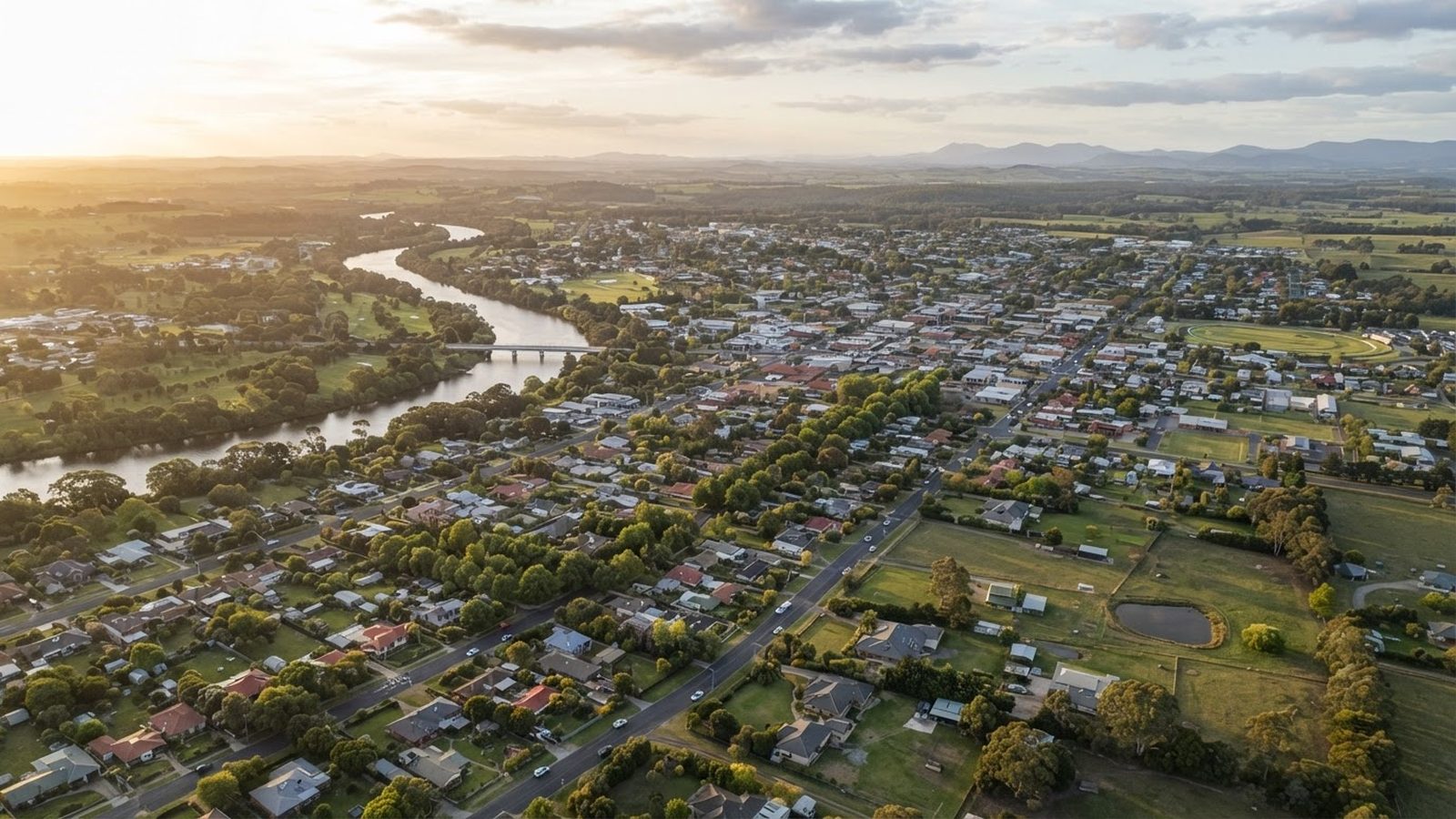 Wide aerial photograph of East Gippsland residential landscape near Bairnsdale at golden hour, showing acreage properties, the Mitchell River corridor, and the modern suburban fringe including Eastwood and Shannon Waters Estate.